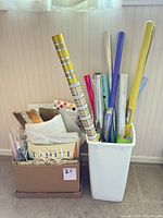 Box of gift bags, tissue paper and gift boxes beside bin holding wrapping paper rolls