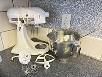 White KitchenAid mixer with bowl, pouring shield and three attachments displayed