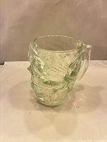 Oblique view of clear glass skull mug showing handle and relief detail