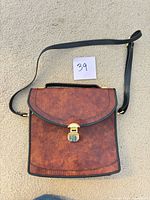 front view showing brown wood-grain leather, curved flap, gold-tone clasp, black strap