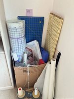 Overview of box with cutting mats, rolled interfacing, thread stand with cones, blue storage case and assorted tools