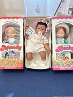 Front view of three dolls: Mandy and Becky boxed, Gotz infant doll centered