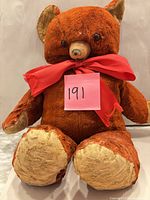 Front view of vintage red-brown plush teddy bear with rubber snout and wear on paws