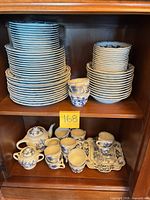 Stacks of plates, bowls, cups, teapot, creamer, sugar, platter in cabinet