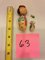 Three wooden kokeshi dolls next to measuring tape and sticky note 63