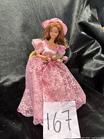 Barbie doll wearing pink lace dress and hat, holding tulip bouquet, seated on wicker chair