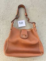 Front view of Dooney & Bourke British tan leather feed bag with adjustable strap and logo flap
