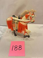 Left side view of horse figurine showing orange fringe and saddle