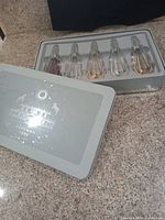 Five Beekman 1802 fragrance bottles in open metal tin on countertop