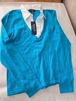 Front view of turquoise pullover with white collar and hangtag