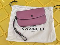 Coach purple wristlet resting on branded dust bag