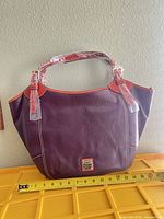 Front view of burgundy and brown Dooney & Bourke leather tote with measuring tape for width