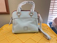 Front view of light mint Dooney & Bourke leather satchel with protective wraps and detachable strap