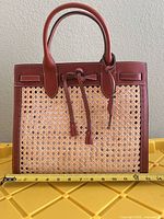 Front view of leather and straw tote with tape for width reference