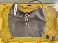 Full view of olive Dooney & Bourke hobo bag with measuring tape for scale and retail tag attached