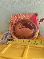 Front view of small Dooney & Bourke paint-splatter leather crossbody bag with ruler for scale and wrapped strap visible