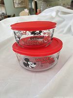 Two stacked glass containers with Mickey Mouse graphics and red lids