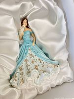 Full view of figurine lying on white satin showing gown colors and fan