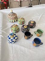 Group shot of six lidded jars and two mugs on table