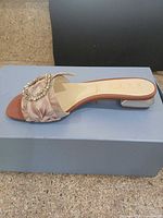 Side view of one sandal on box showing upper fabric, buckle and heel