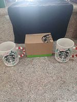 Two holiday mugs with candy cane handles flanking boxed Las Vegas mug