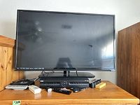 Front view of Vizio 42-inch TV on stand with DVR box and remotes below