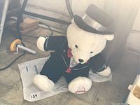 Full view of seated white plush bear in tuxedo and top hat