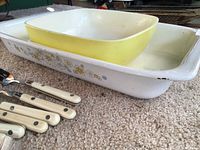 CorningWare roaster with floral pattern and Pyrex yellow square bowl nested inside; portion of other utensils visible but not part of lot