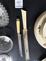 Two serrated knives side by side with plates for scale