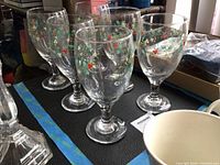 Six clear glass goblets with Winterberry holly design on dark surface