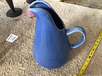 Full view of blue pitcher standing upright beside measuring tape