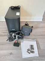 Full system view showing subwoofer, both satellite speakers, interface module, manual, cables