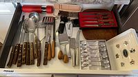 Open drawer showing boxed Portmeirion teaspoons, boxed red-handled knife set, loose wooden utensils and knives