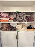 Cabinet showing folded comforters, sheets, towels, plaid textile, storage basket, bamboo tray with blood pressure monitor