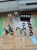 Overview of candlesticks, napkin rings in box and loose, and spoons laid on floor