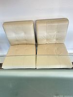 Four cream leather dining chairs side by side backs against wall