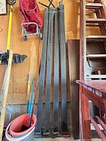 Four long square steel posts leaning against wall with bases visible