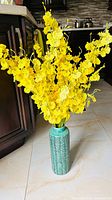 Full view of turquoise vase filled with yellow faux flowers
