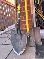 Four shovels leaning against wall showing blade types and handle materials
