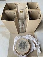 Box with four visible tall clear glasses in cardboard divider and stack of silver-plated coasters on tissue