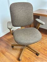 Front view of brown upholstered swivel office chair showing seat, back, armrests and wooden base on casters