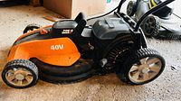 Side view of orange Worx 40V cordless lawn mower showing deck, wheels, battery cover and handle