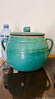 Front view of turquoise glazed pottery jar with lid and handles