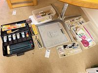 Overview of all craft supplies on floor including carry case, four tubs, paint bottles, beads and tools