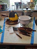 Overview of yellow fondue set, white ceramic fondue pot, stainless chafing pot and group of fondue forks