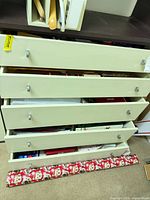 Drawer unit with multiple open drawers showing wrapping supplies, Santa print wrapping paper roll visible