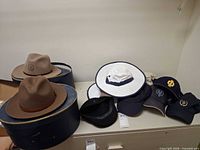 Overview of two Stetson hats on hat boxes and assorted caps on shelf