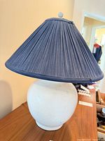 Full view of lamp on table showing blue pleated shade and white ceramic base