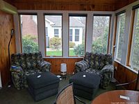 Sunroom view showing both lamps: OttLite table lamp between ottomans, Phive floor lamp beside chair
