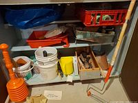 Cabinet shelves showing trays, buckets, drop cloth and assorted tools